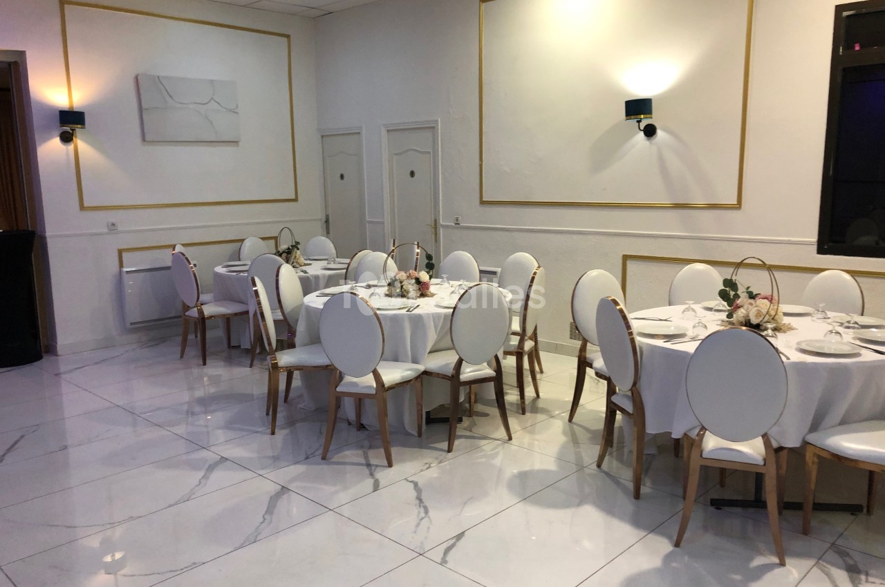 Salle de réception lumineuse avec tables rondes dressées, chaises blanches et décorations florales.