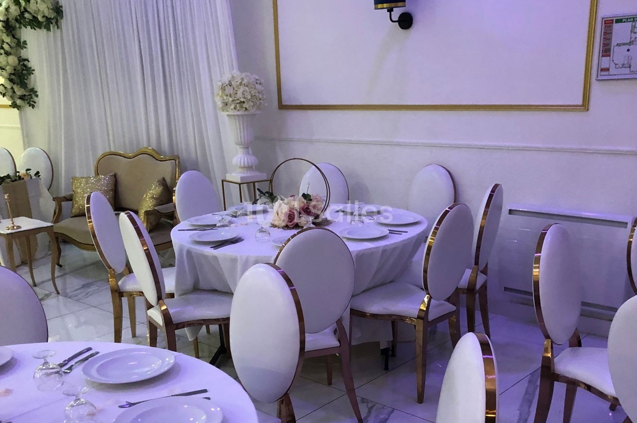 Salle de réception élégante avec tables dressées, chaises blanches et décorations florales dans un cadre lumineux.