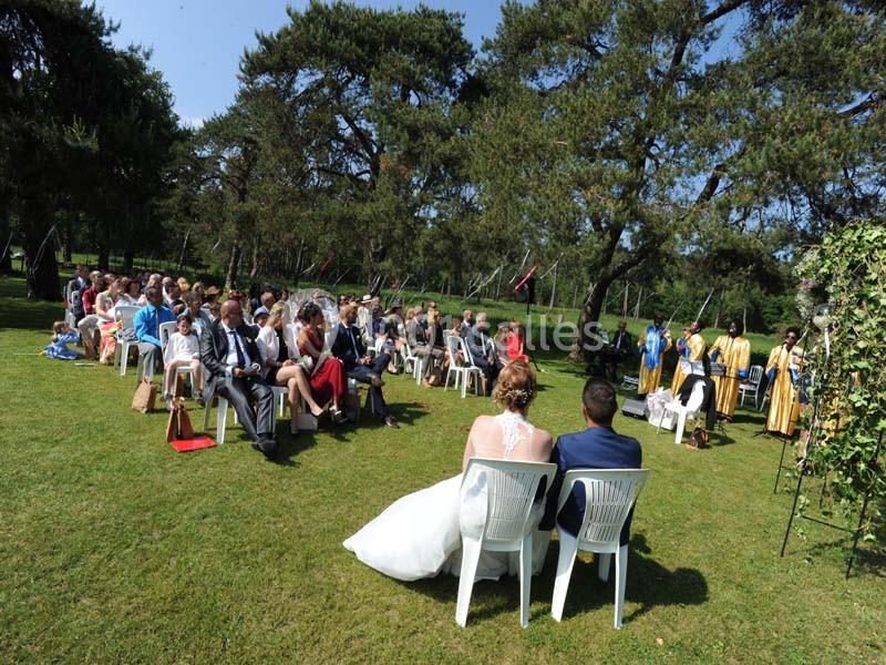 Cérémonie de mariage en plein air avec des invités assis sur des chaises blanches, entourés d'arbres et de verdure.