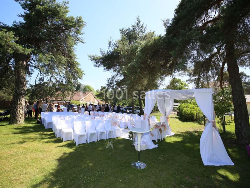 Chaises blanches alignées en extérieur sous des arbres, avec une arche décorée pour une cérémonie en plein air.