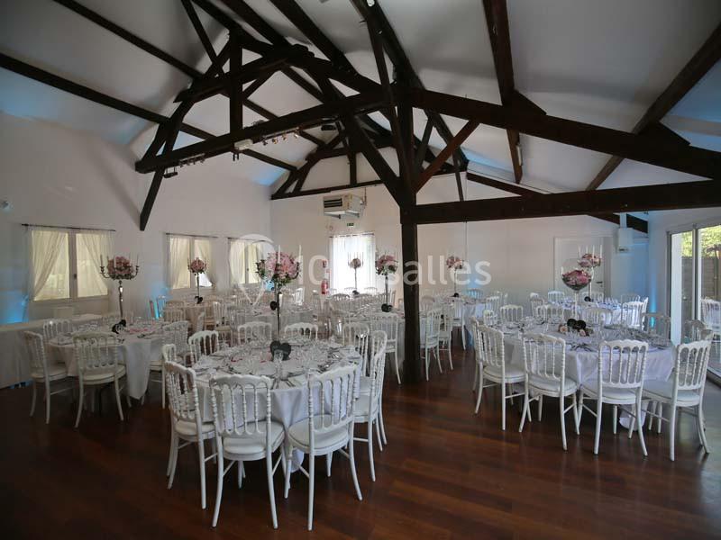 Salle de réception lumineuse avec tables rondes décorées de nappes blanches et centres de table fleuris.