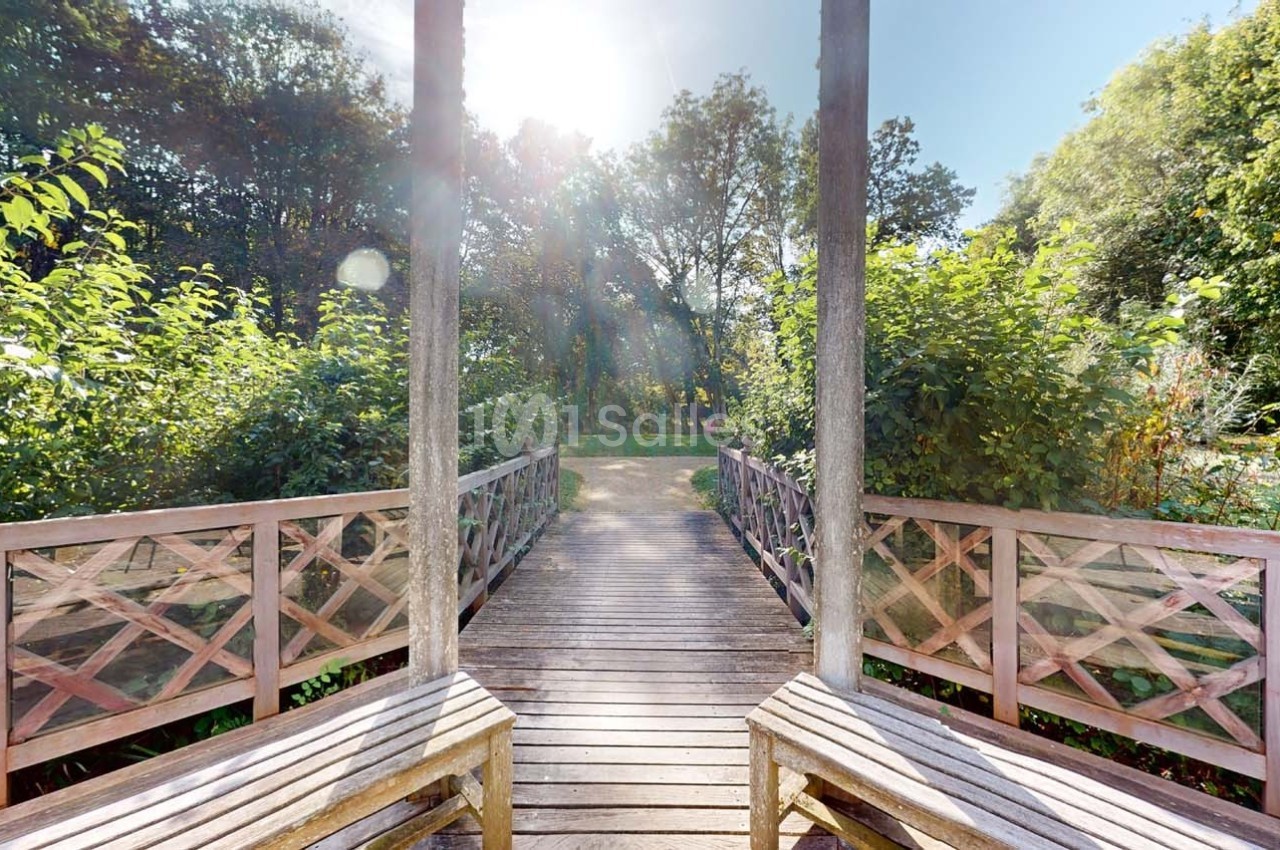 Passerelle en bois bordée de végétation, éclairée par le soleil à travers les arbres.