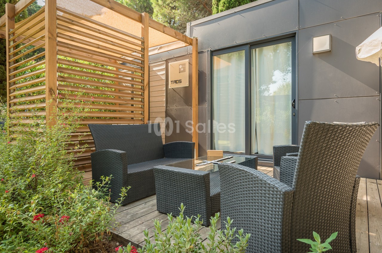 Mobilier de jardin en résine tressée sur une terrasse en bois, entourée de végétation et attenante à un logement moderne.