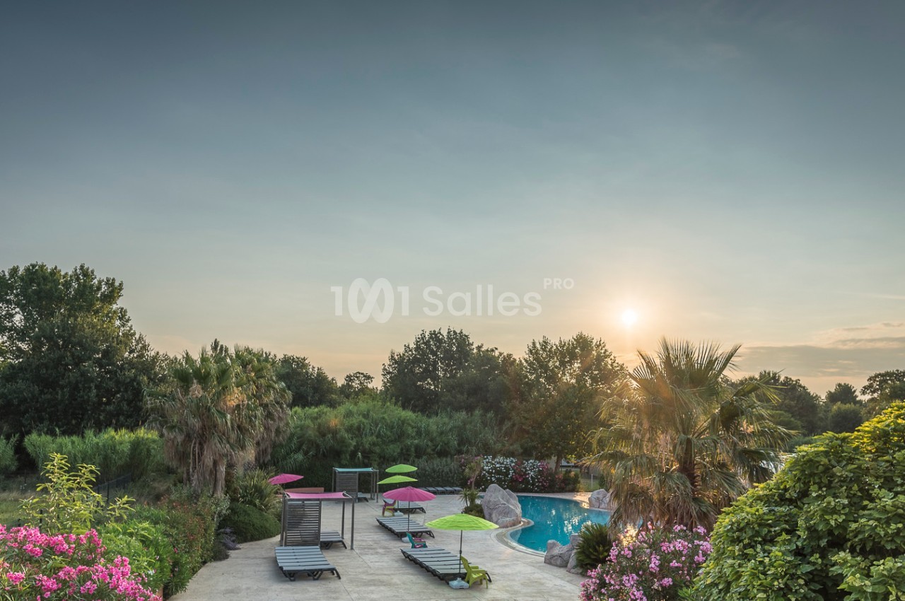 Piscine extérieure entourée de chaises longues, parasols colorés, végétation luxuriante et coucher de soleil.