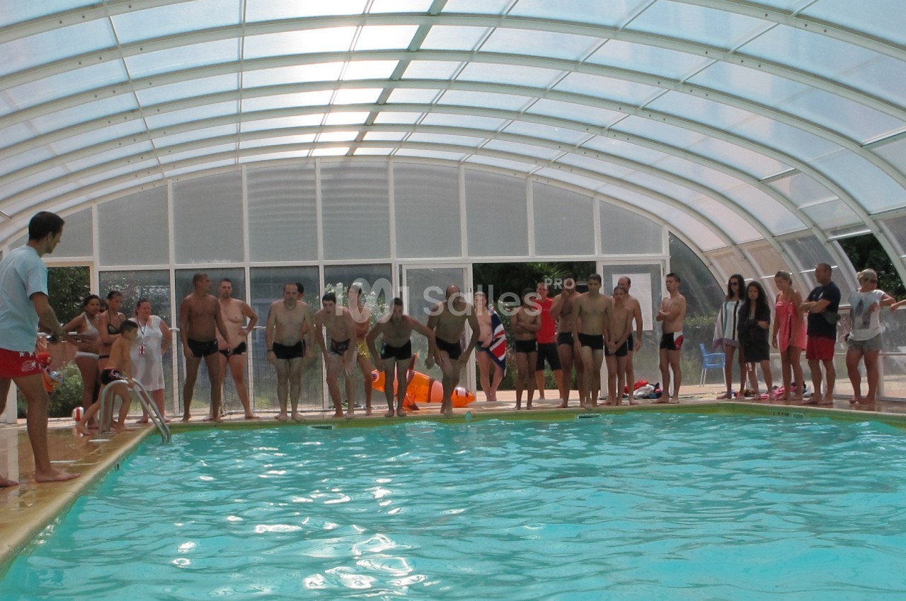 Des personnes en maillot de bain alignées au bord d'une piscine couverte, prêtes à plonger, avec des spectateurs en arrière…