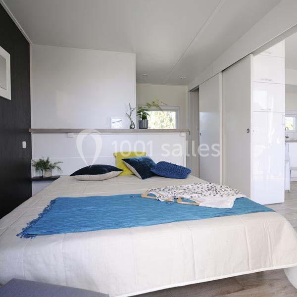 Chambre lumineuse avec lit double, couverture bleue, coussins colorés et placards blancs coulissants.