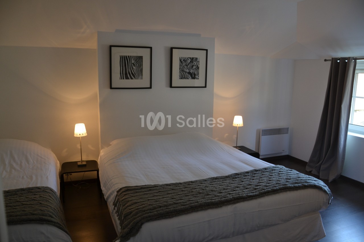Chambre avec un lit double, un lit simple, deux lampes de chevet allumées et une fenêtre avec rideaux gris.