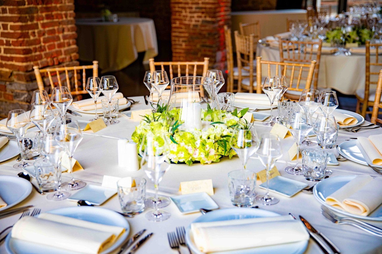 Table élégamment dressée avec nappes blanches, centre de table floral et verres disposés pour un événement formel.