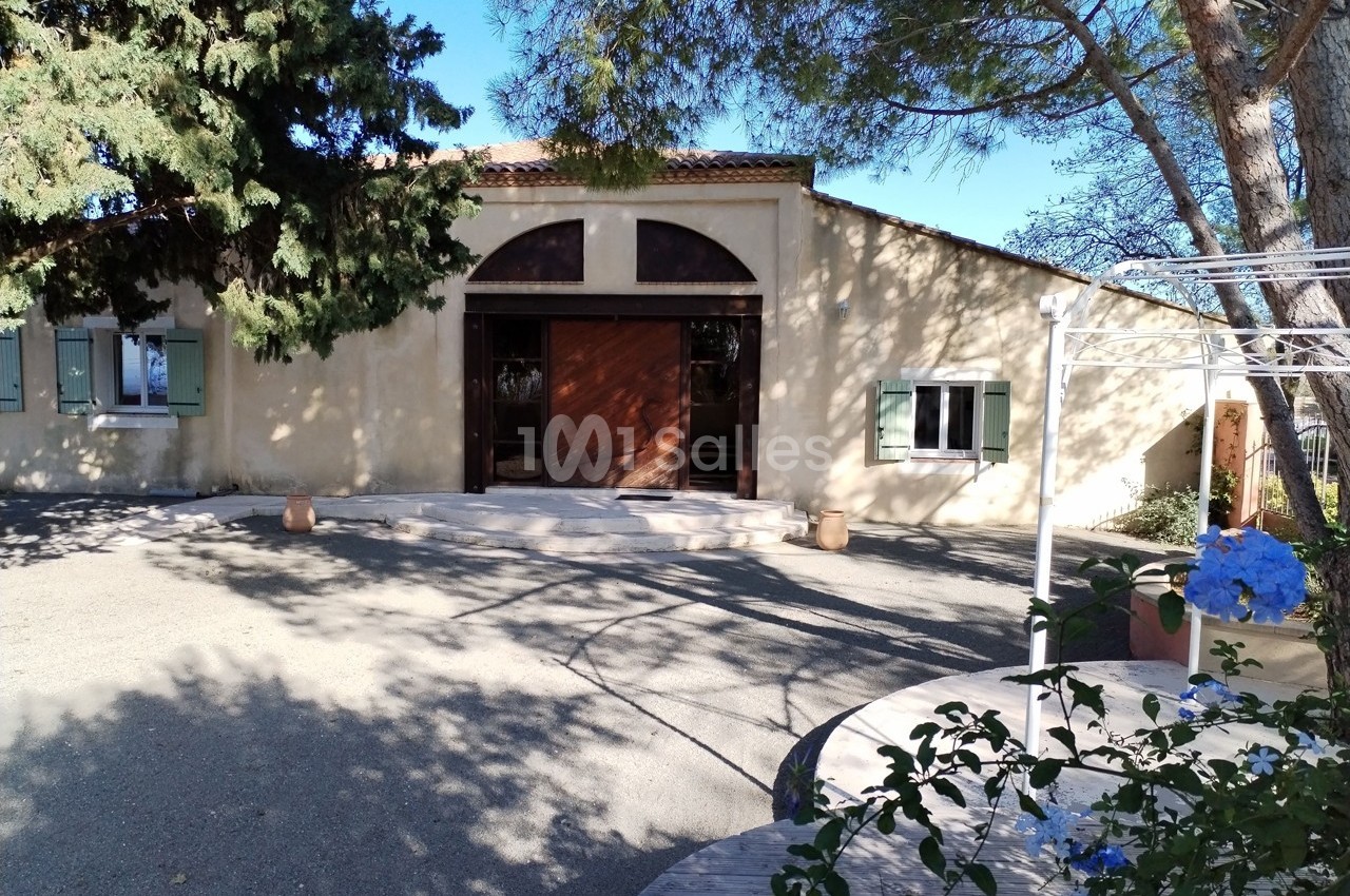 Façade d'un bâtiment en pierre avec porte en bois, entouré d'arbres et d'un espace extérieur ombragé.