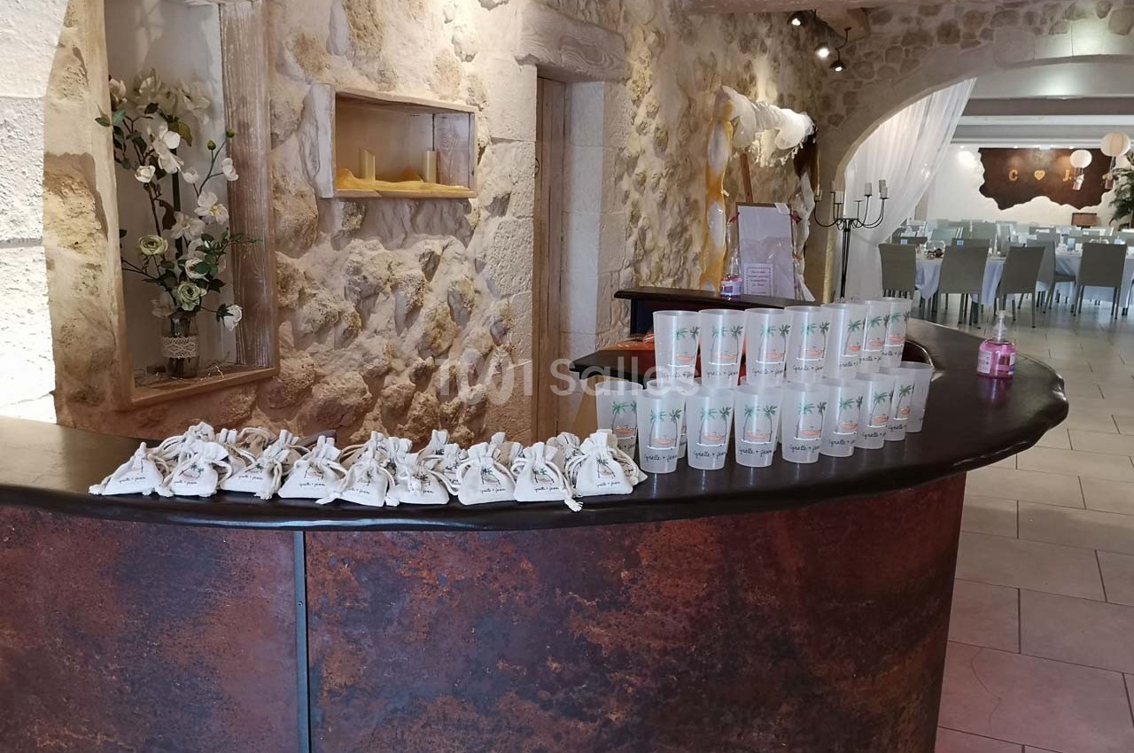 Comptoir en bois sombre avec des cadeaux et gobelets alignés, dans une salle en pierre décorée pour un événement.