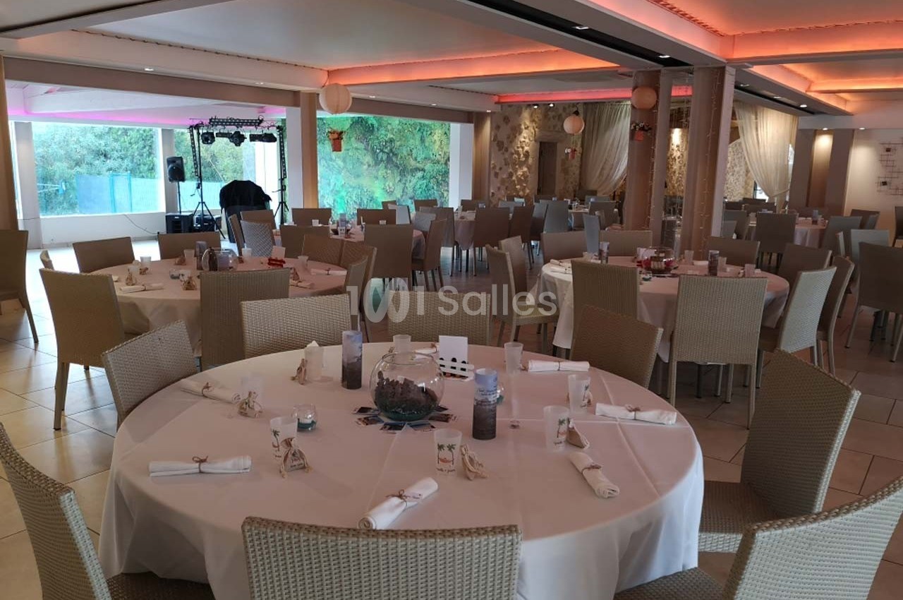 Salle de réception lumineuse avec tables rondes dressées, chaises en osier et décorations sobres.