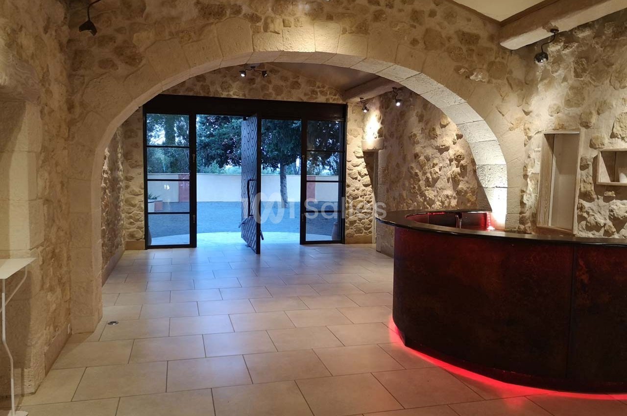 Salle avec murs en pierre, comptoir arrondi éclairé en rouge et grande ouverture vitrée donnant sur l'extérieur.