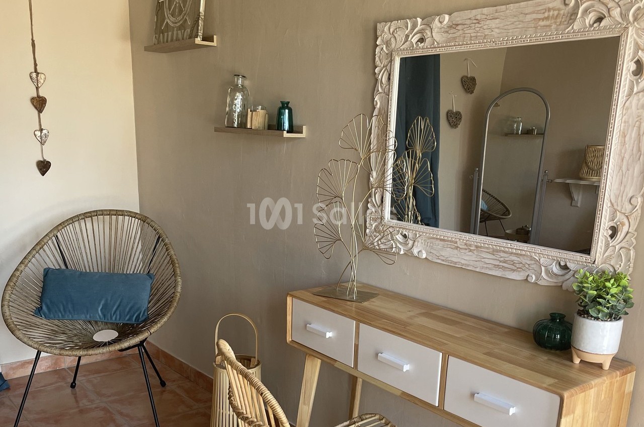 Coin de décoration intérieure avec un miroir encadré, une console en bois, une chaise en rotin et des éléments décoratifs.