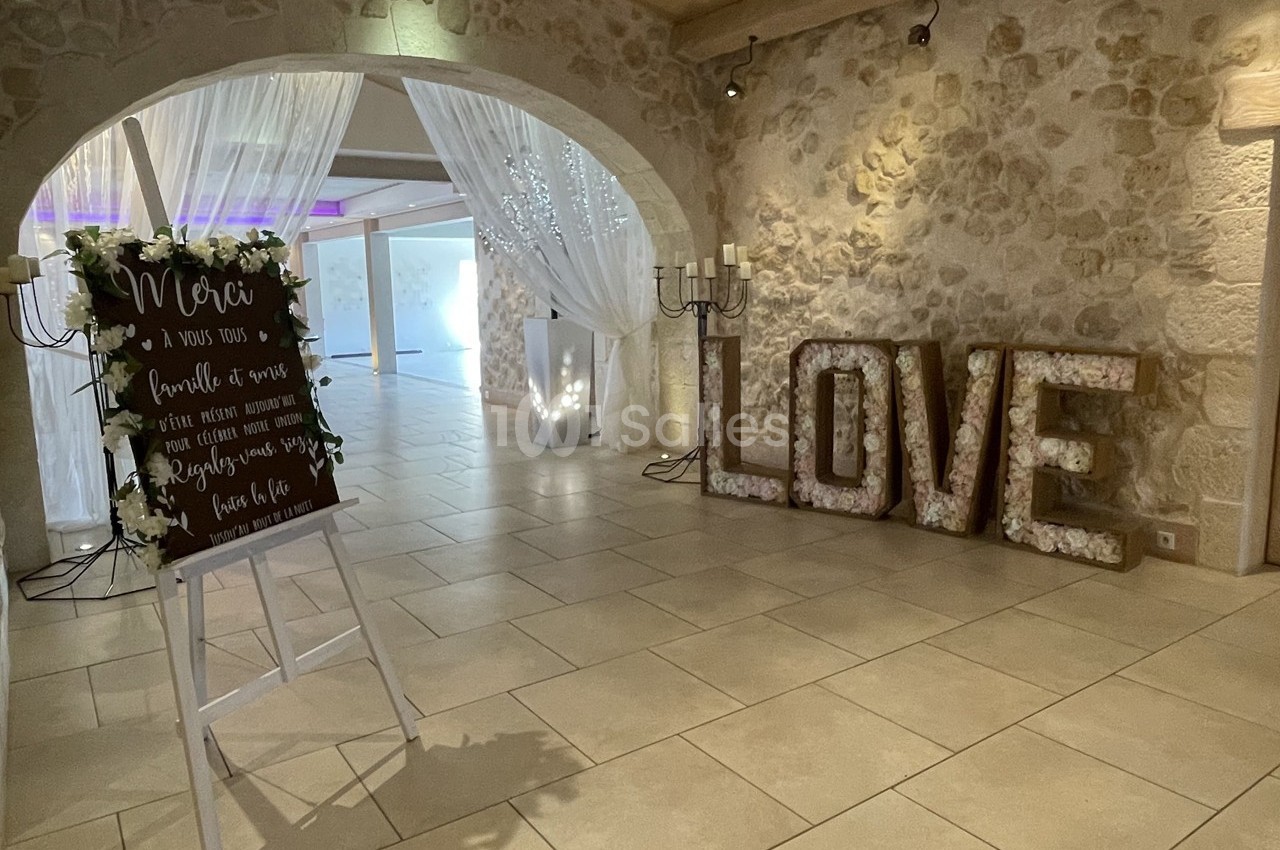 Salle de réception décorée avec un panneau de remerciement, des rideaux lumineux et des lettres ’LOVE’ illuminées.
