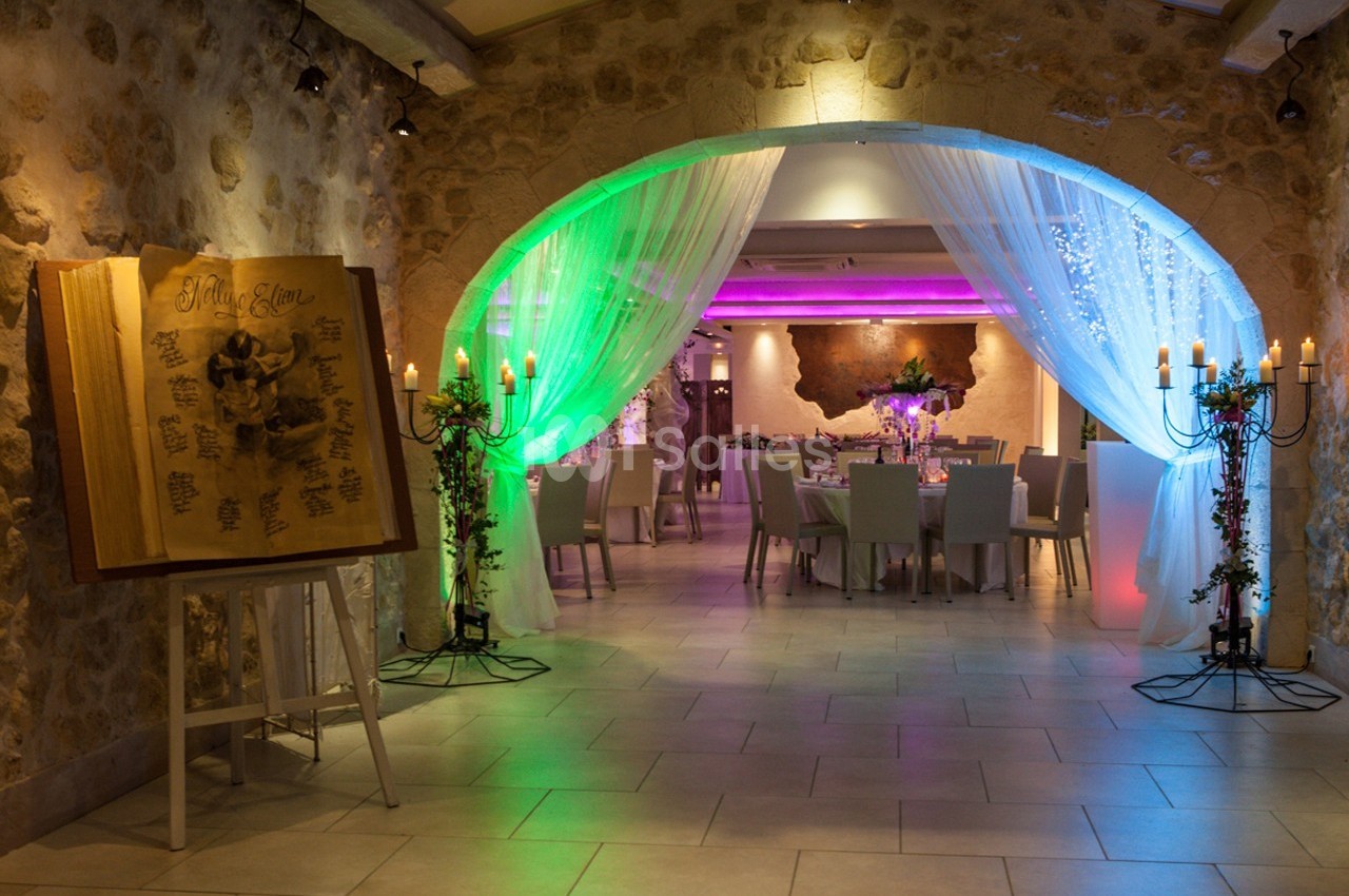 Salle de réception décorée avec des tables dressées, éclairage coloré et un grand livre d'honneur sur un chevalet.