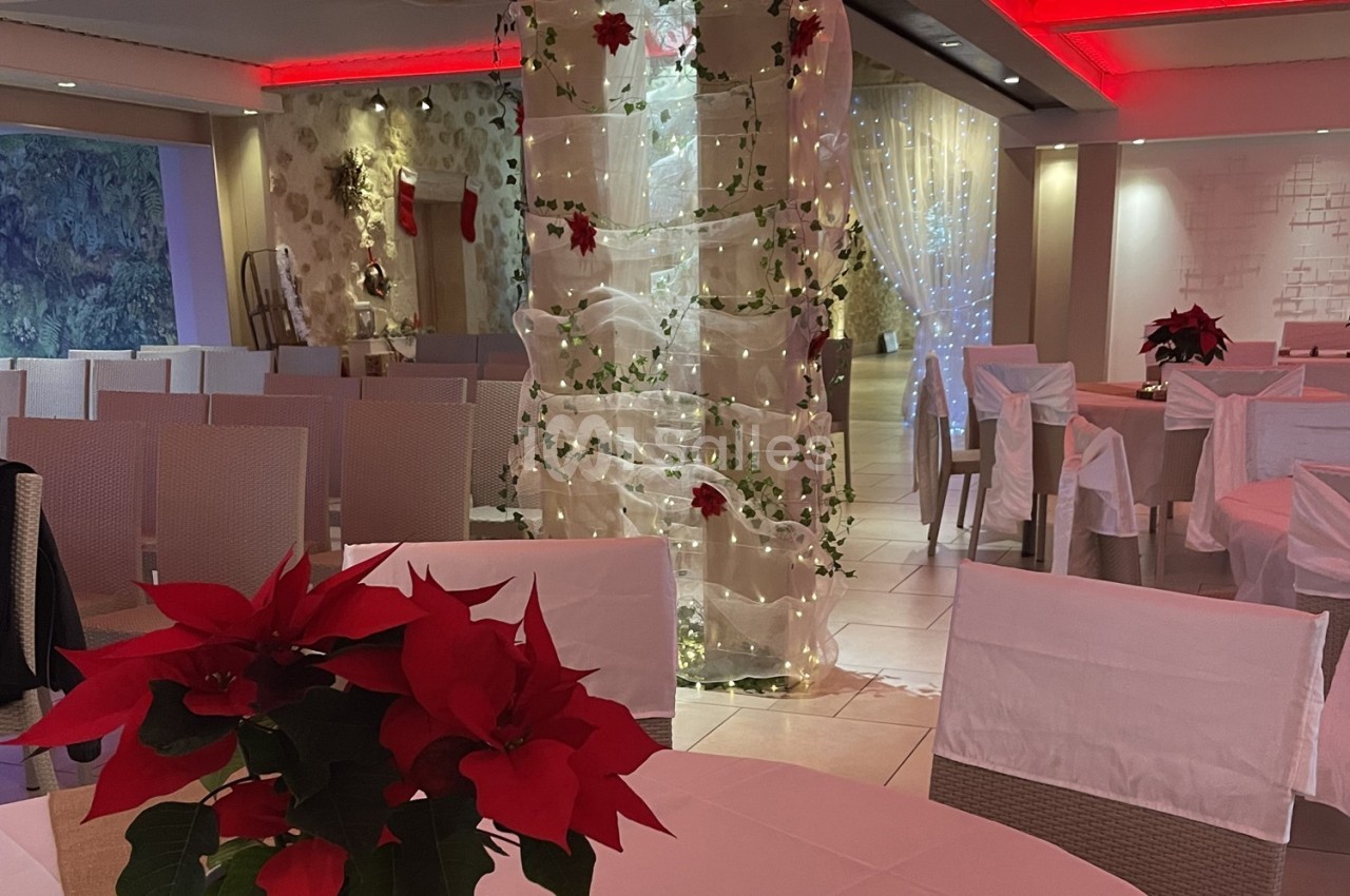 Salle décorée pour un événement, avec des chaises alignées, des poinsettias rouges et des guirlandes lumineuses.
