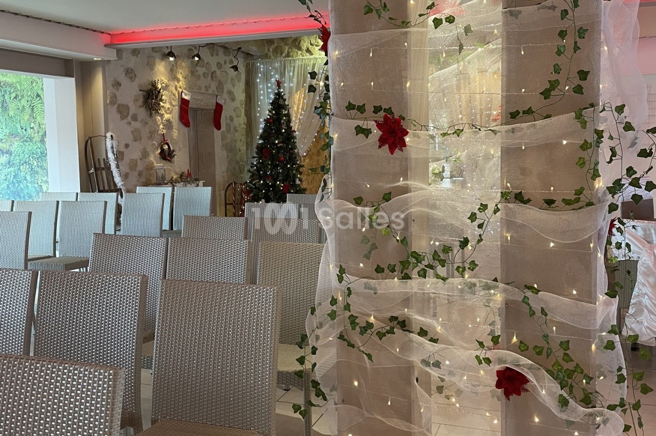 Salle décorée pour Noël avec des chaises alignées, un sapin illuminé et des guirlandes ornées de feuillage et de fleurs…