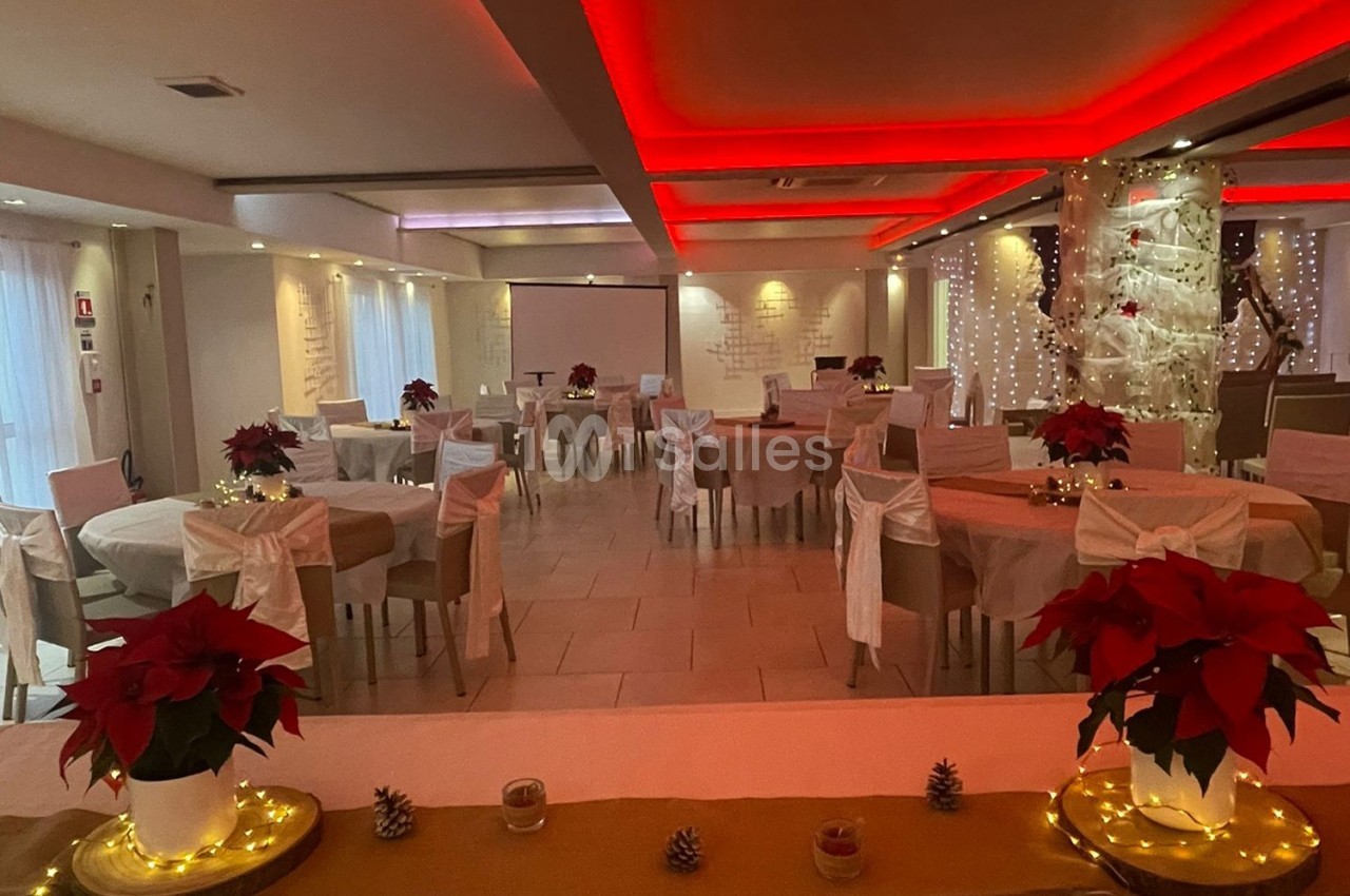 Salle de réception décorée pour une fête, avec tables rondes, nappes beige, chaises blanches et poinsettias rouges.