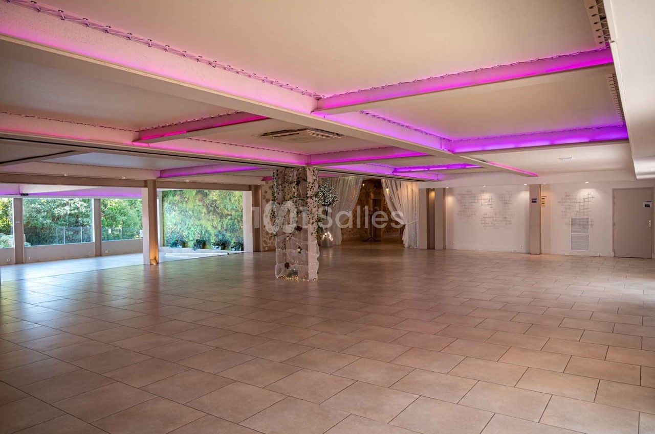 Salle spacieuse avec carrelage clair, éclairage LED violet au plafond et grandes baies vitrées donnant sur un jardin.