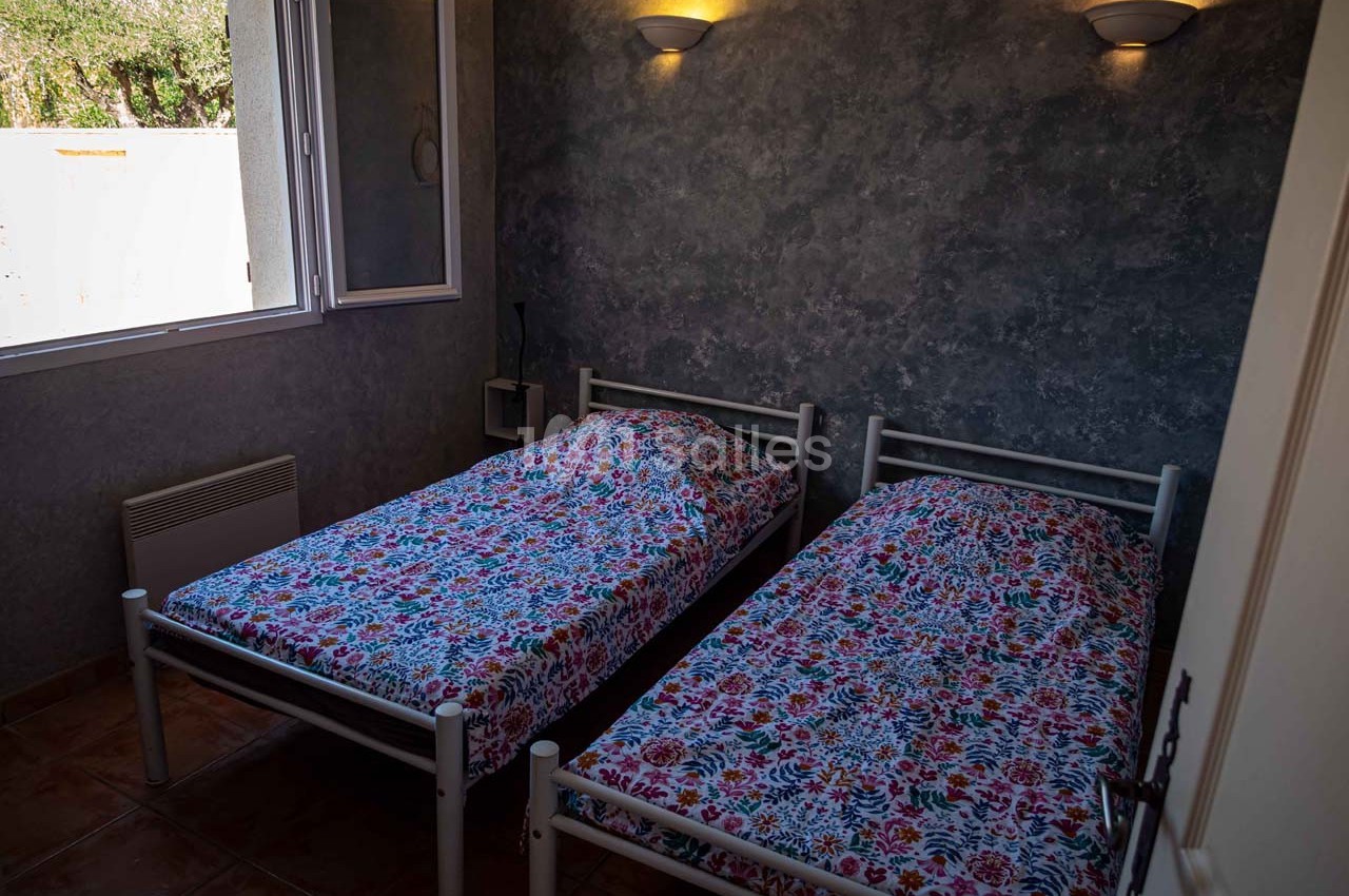 Deux lits simples avec des draps à motifs colorés dans une chambre sombre, éclairée par des appliques murales.