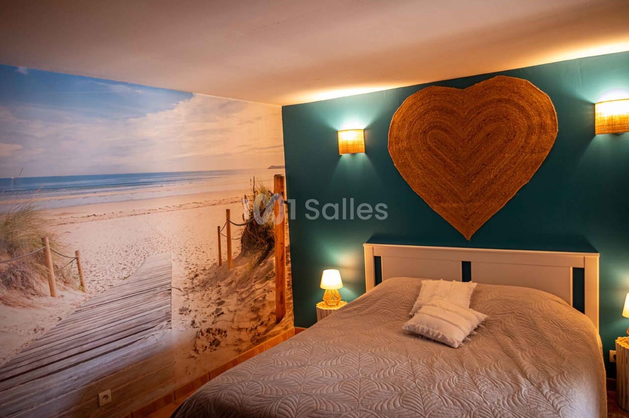Chambre avec un lit double, mur décoré d'une photo de plage et éclairage doux avec appliques et lampes de chevet.