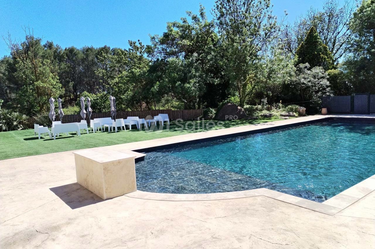 Piscine extérieure entourée de verdure avec des chaises blanches et des parasols sur une pelouse.