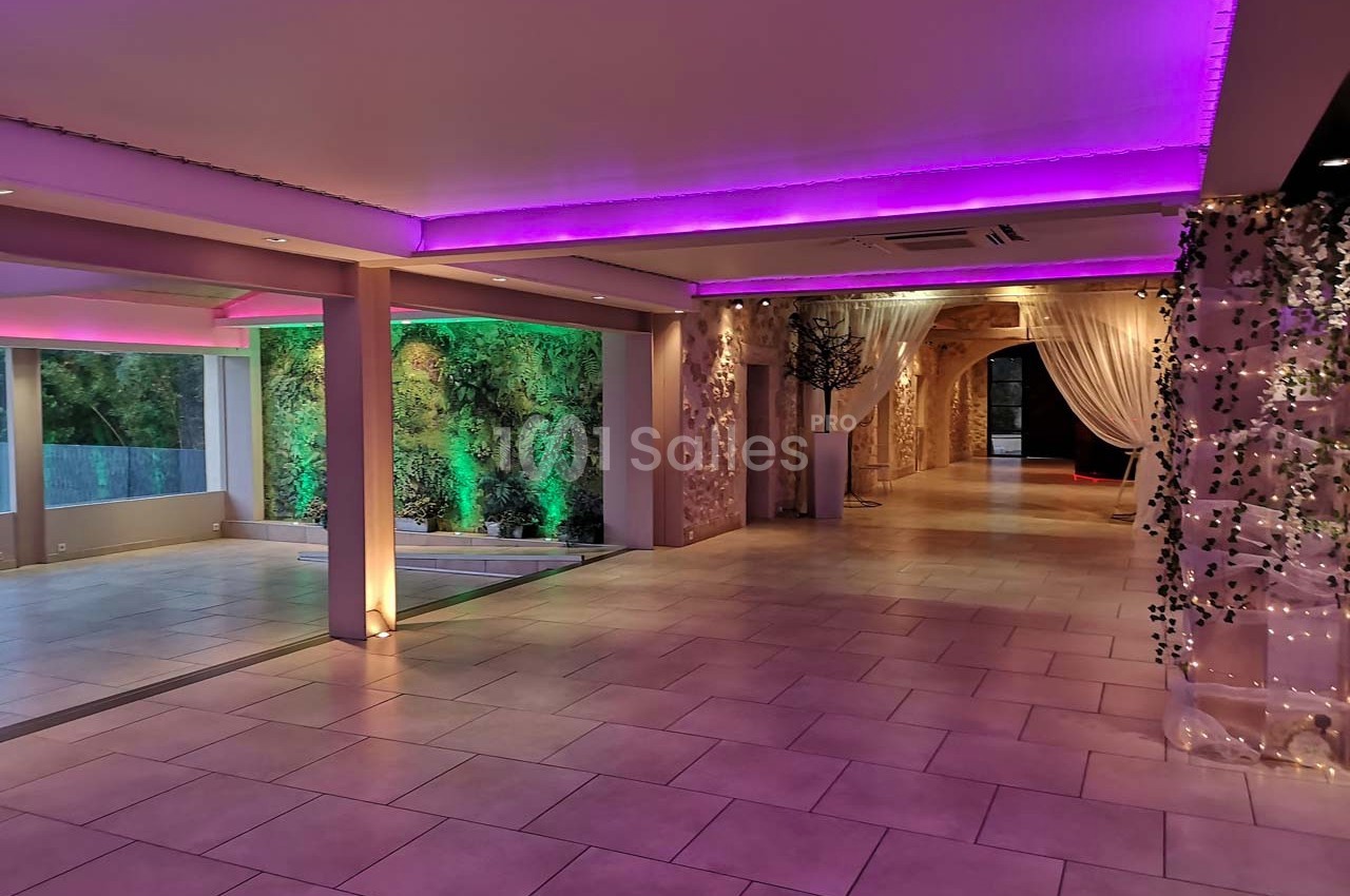 Salle spacieuse avec éclairage LED violet, murs végétalisés et rideaux blancs créant une ambiance élégante.