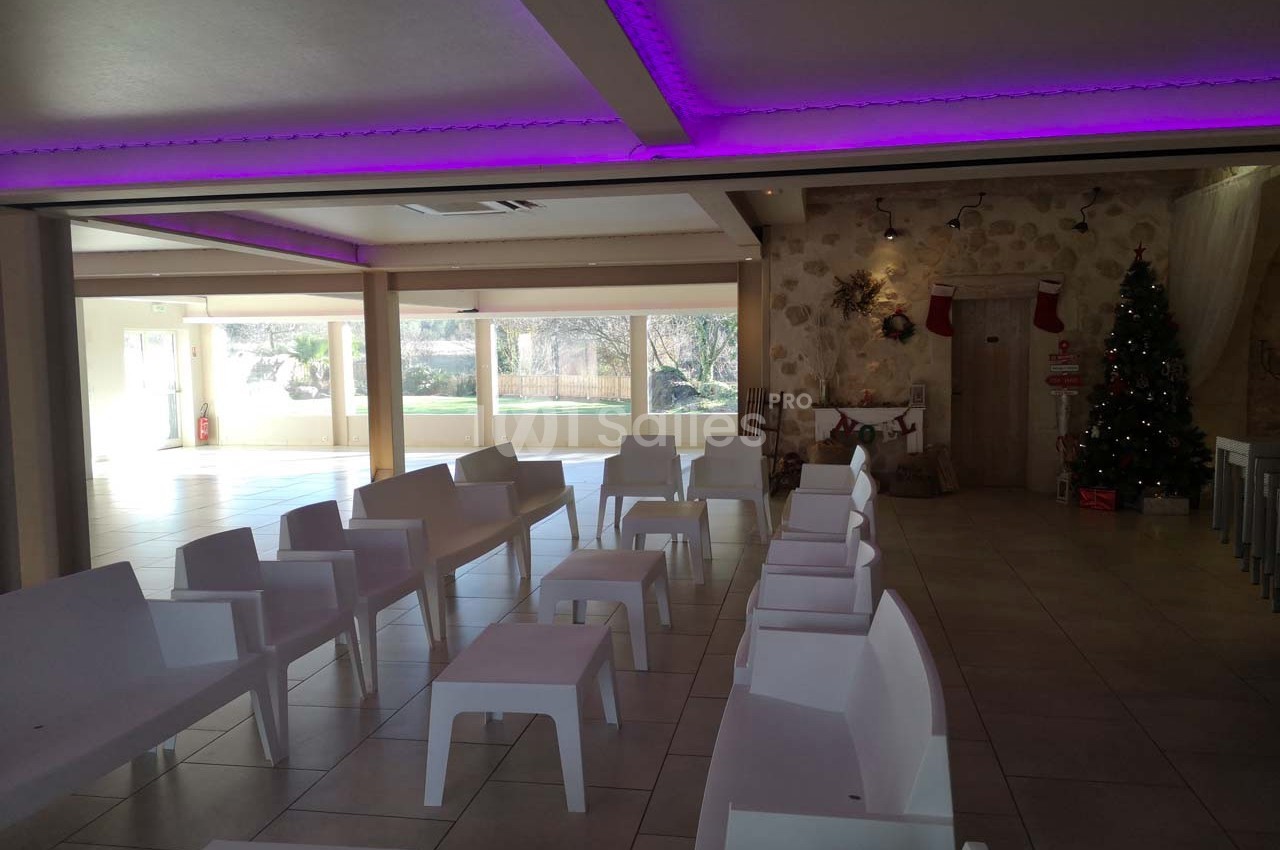 Salle lumineuse avec chaises blanches alignées, décorations de Noël et vue sur un jardin à travers de grandes baies vitrées.