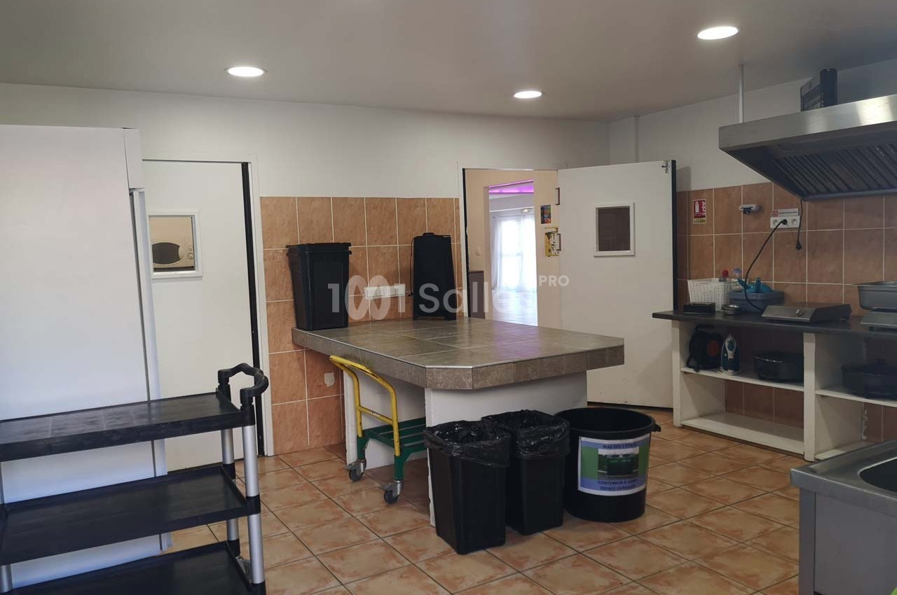 Cuisine professionnelle avec plan de travail central, étagère roulante, poubelles et équipements de cuisson.