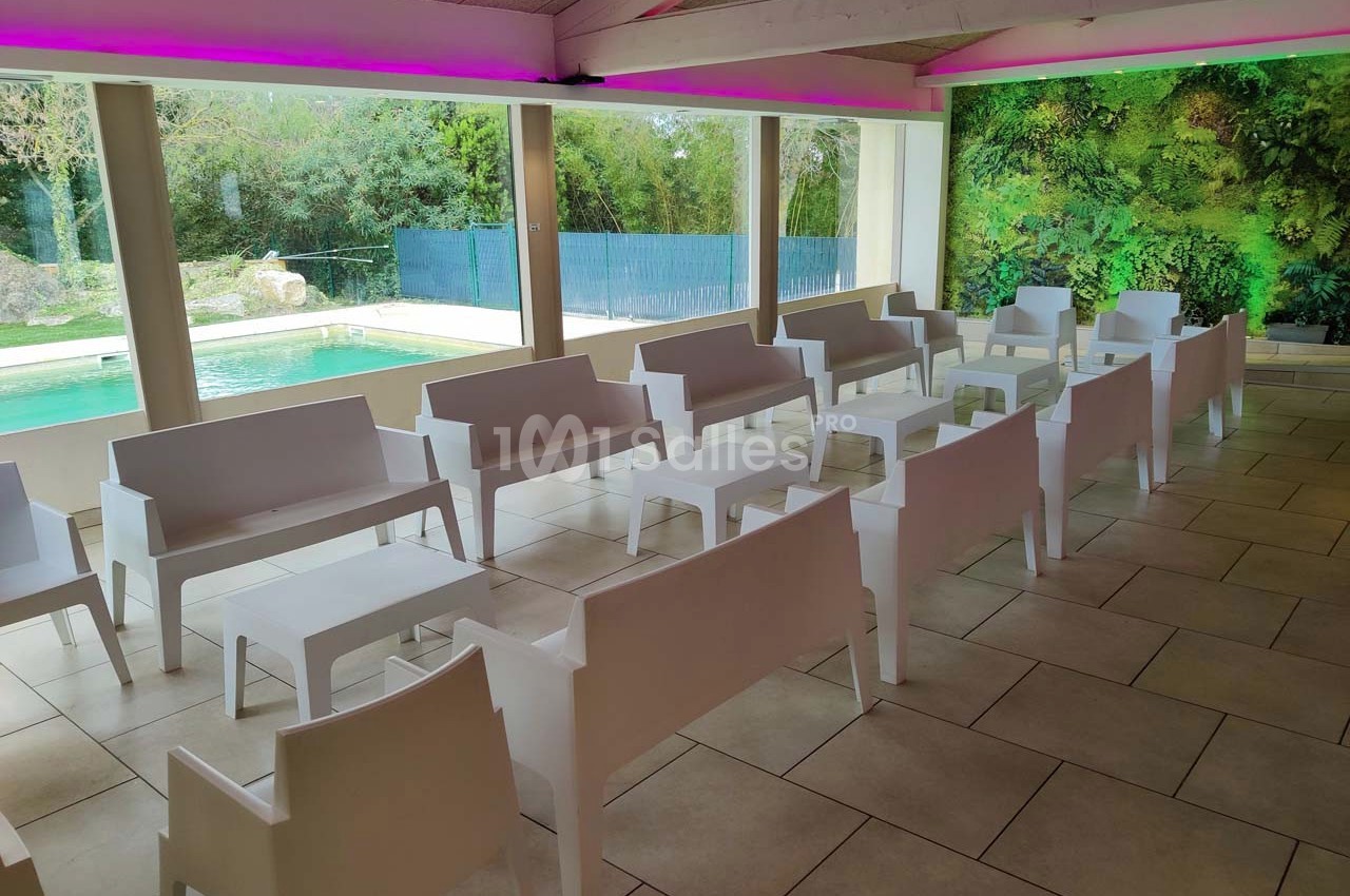 Salle lumineuse avec des bancs blancs alignés, vue sur une piscine et un mur végétal en arrière-plan.