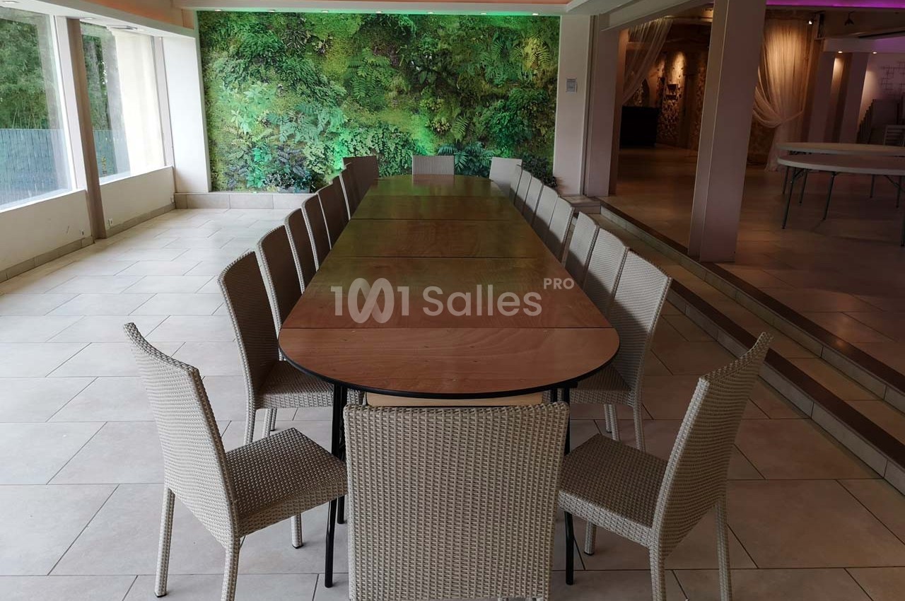 Table rectangulaire en bois entourée de chaises en rotin dans une salle lumineuse avec un mur végétal en arrière-plan.