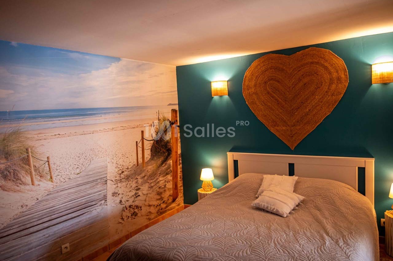 Chambre avec un lit double, mur décoré d'une photo de plage et éclairage doux avec appliques et lampes de chevet.