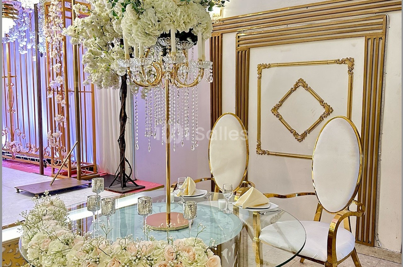 Table décorée avec des fleurs blanches et roses, chandelier doré orné de cristaux, deux chaises blanches élégantes.