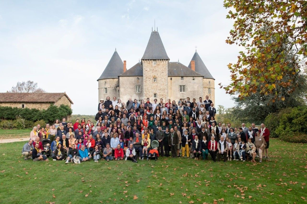 Un grand groupe de personnes posant devant un château historique entouré de pelouses et d'arbres en automne.