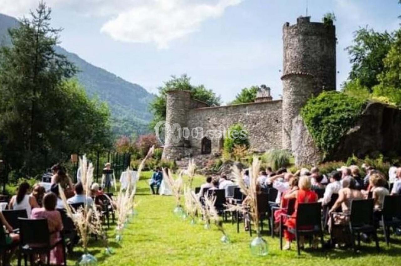 Cérémonie en plein air avec des invités assis, face à un officiant, près d'un château entouré de verdure.