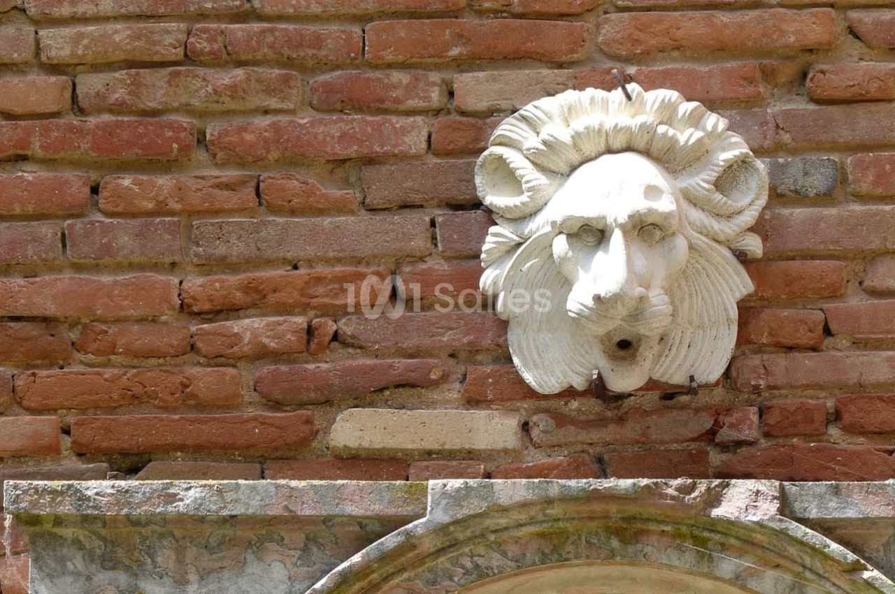 Bas-relief en pierre représentant une tête de lion sculptée, fixé sur un mur de briques rouges.