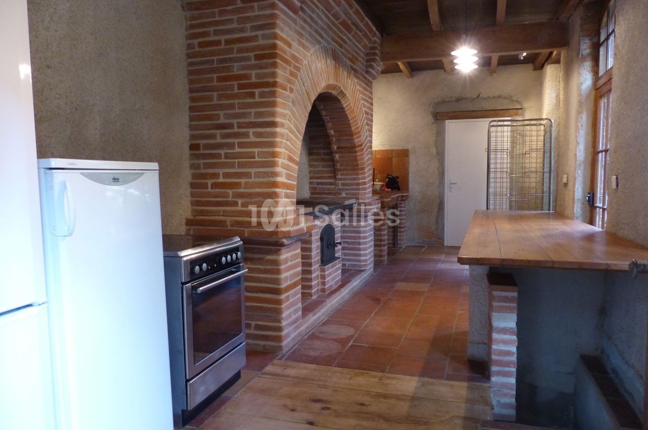 Cuisine rustique avec murs en briques, four encastré, plan de travail en bois et sol en carreaux de terre cuite.