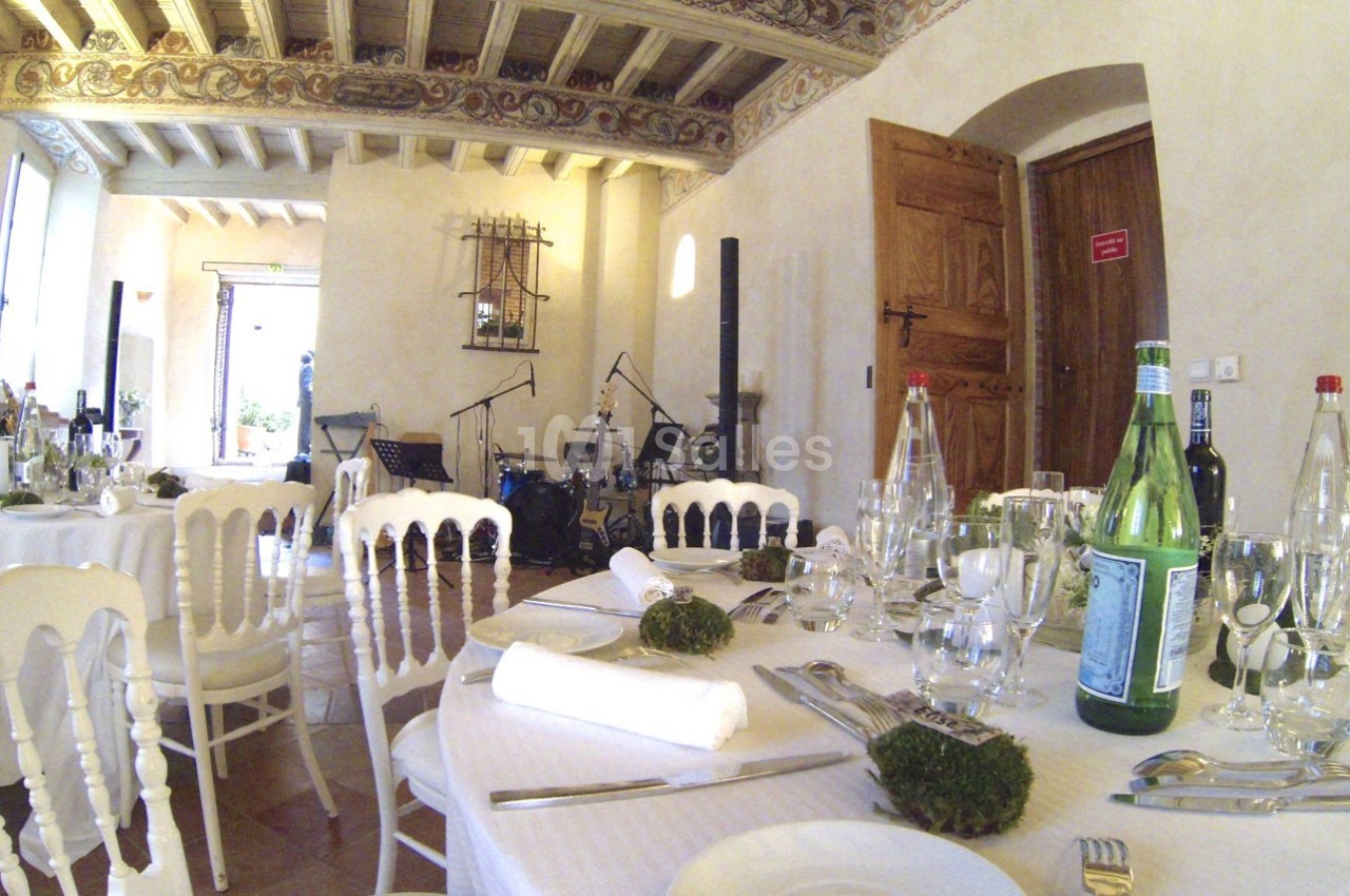 Salle de réception élégante avec tables dressées, chaises blanches et un espace musical équipé de micros et instruments.