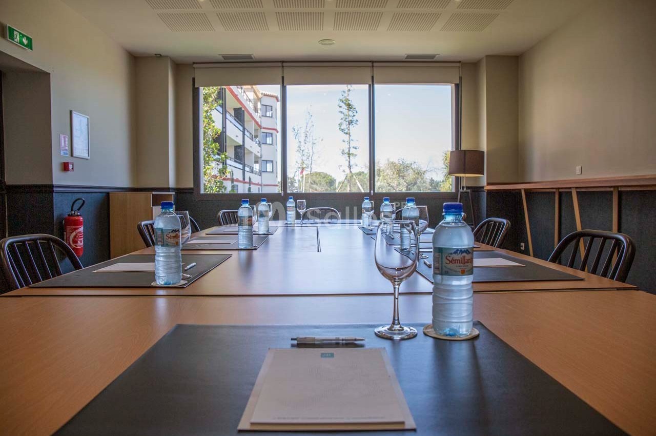 Salle de réunion lumineuse avec une grande table, des chaises, des bouteilles d'eau et des blocs-notes disposés.