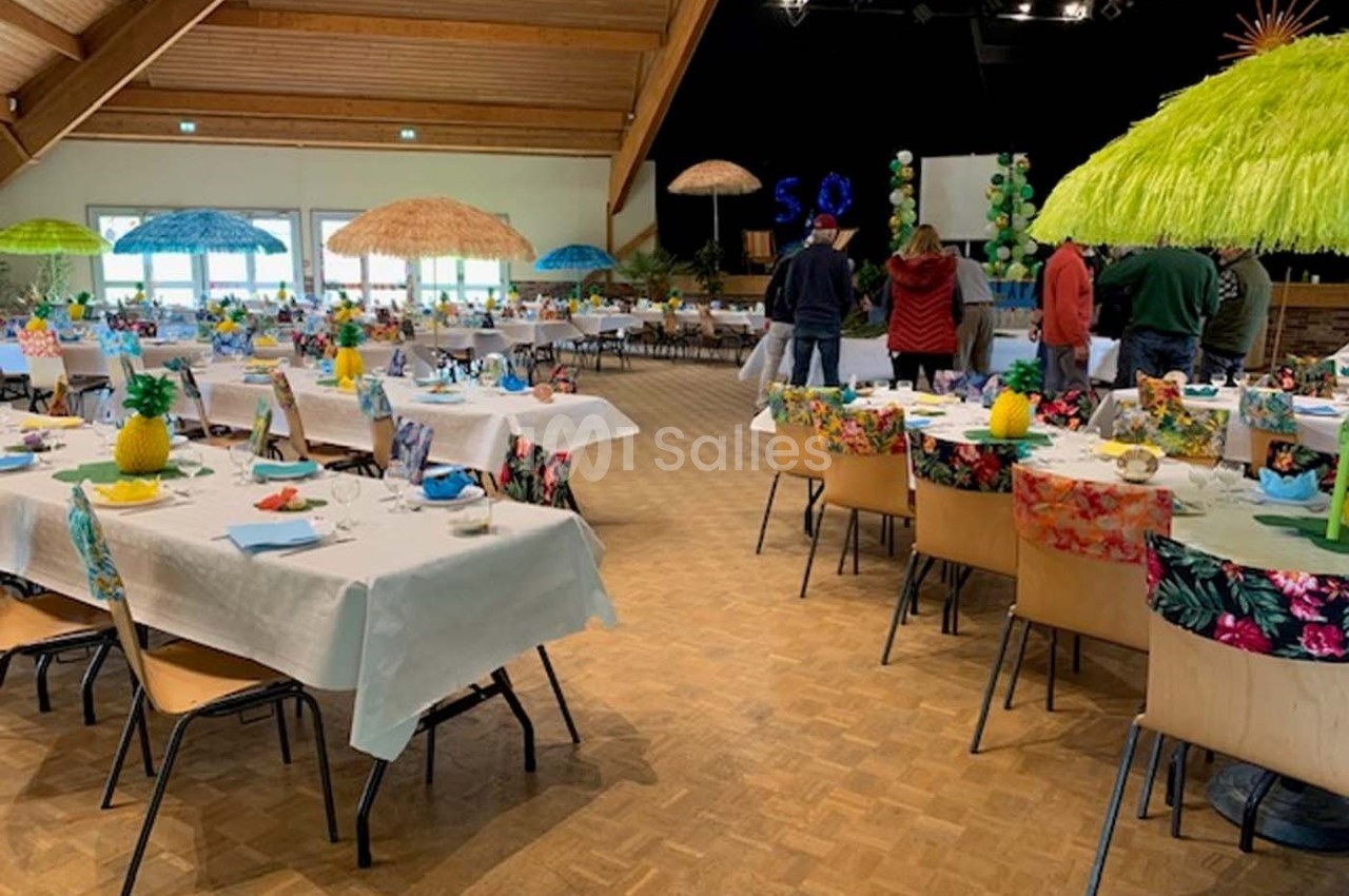 Salle décorée sur un thème tropical avec tables dressées, nappes colorées et parasols en paille.