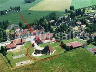 Vue aérienne d'un village avec des bâtiments, des espaces verts et un site entouré en rouge pour mise en évidence.