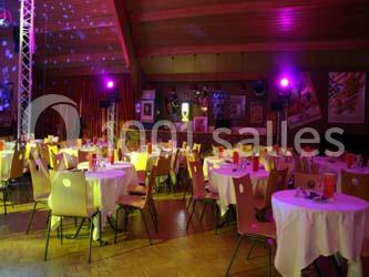 Salle décorée pour un événement, avec des tables rondes dressées et un éclairage tamisé coloré.