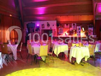 Salle de réception décorée avec des tables rondes dressées, éclairage coloré et ambiance chaleureuse.