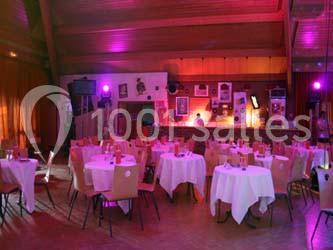 Salle de réception avec tables rondes dressées, éclairage tamisé et bar en arrière-plan.