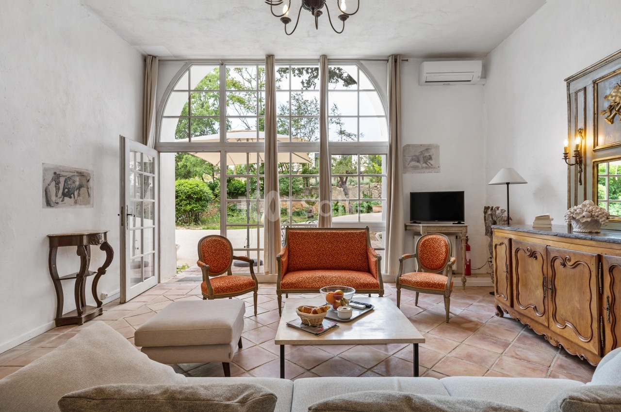 Salon lumineux avec grandes fenêtres cintrées, mobilier classique, et vue sur un jardin verdoyant.