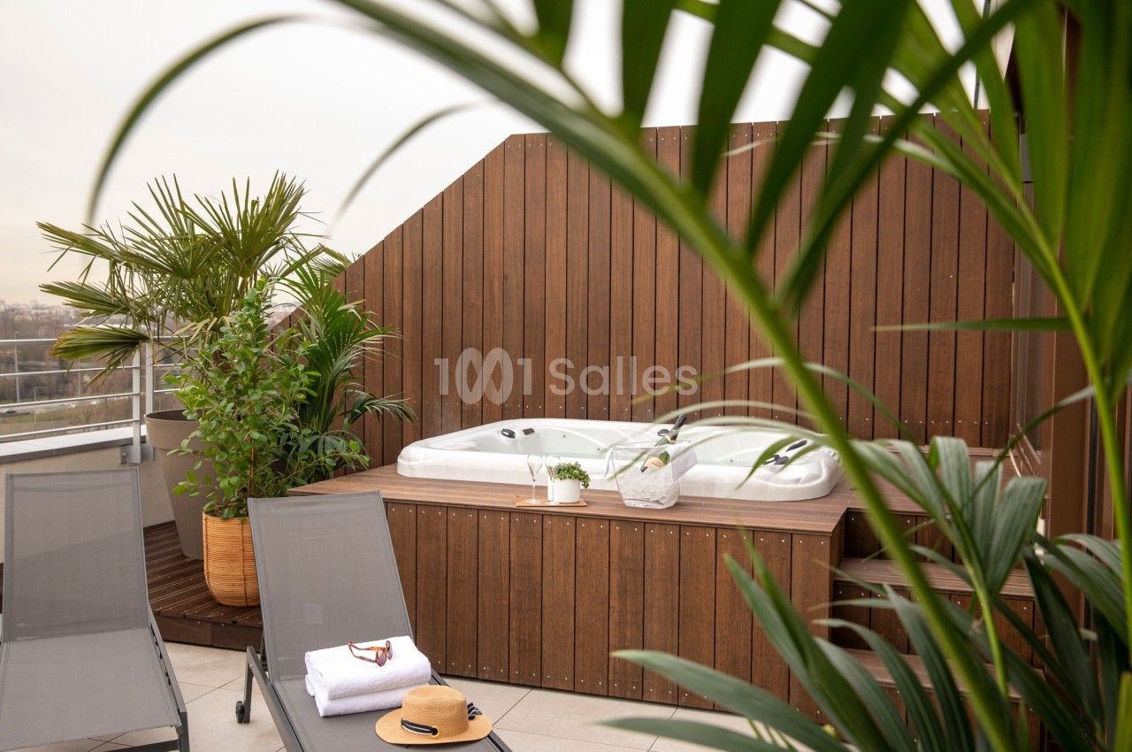 Bain à remous entouré de plantes et de transats sur une terrasse en bois avec vue dégagée.