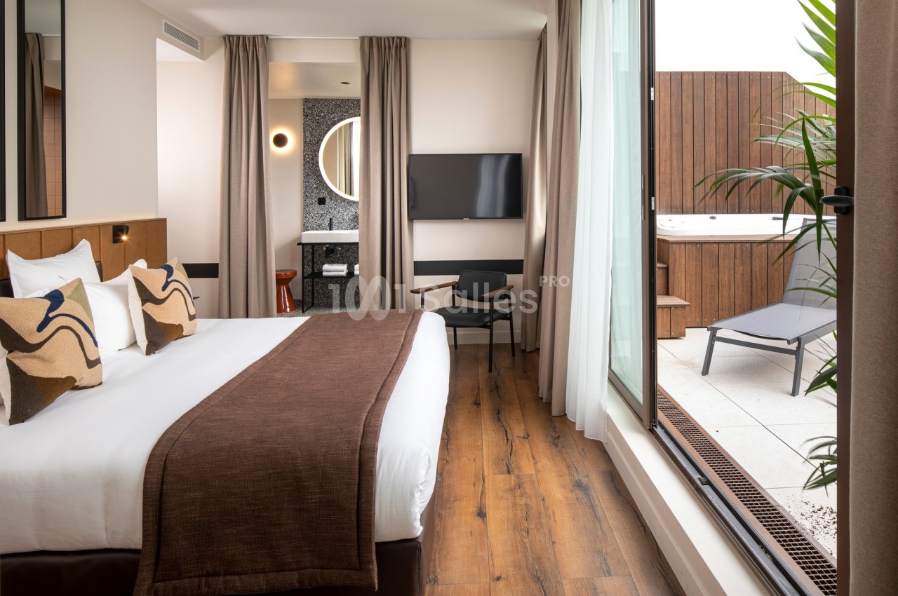 Chambre d'hôtel moderne avec lit double, décoration élégante, télévision, et terrasse équipée d'un jacuzzi et de chaises…