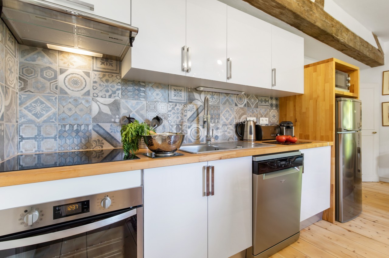 Cuisine moderne avec plan de travail en bois, crédence en carreaux décoratifs, électroménagers inox et rangements blancs.