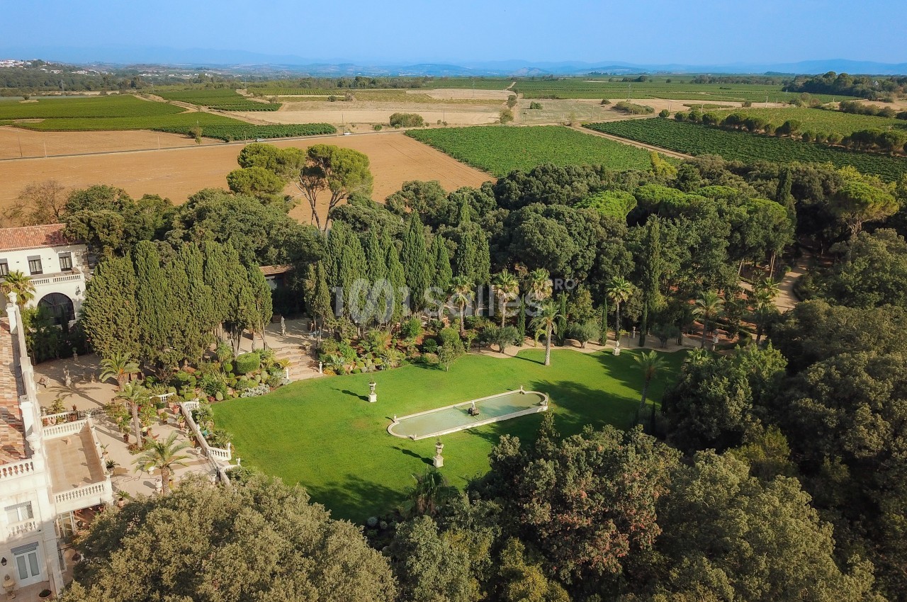 Vue aérienne d'un jardin avec pelouse, bassin central, arbres et paysage de campagne en arrière-plan.
