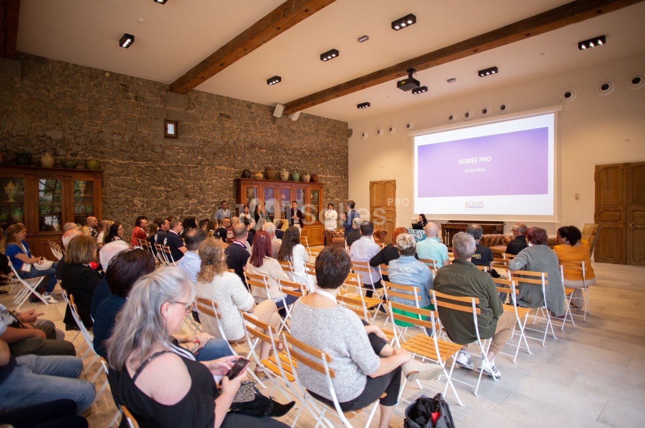 Personnes assises dans une salle de conférence avec un écran projetant une présentation devant un mur en pierre.